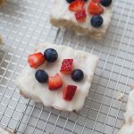 Frosted Berry Sugar Cookie Bars topped with blueberries and strawberry pieces rest on a wire cooling rack.