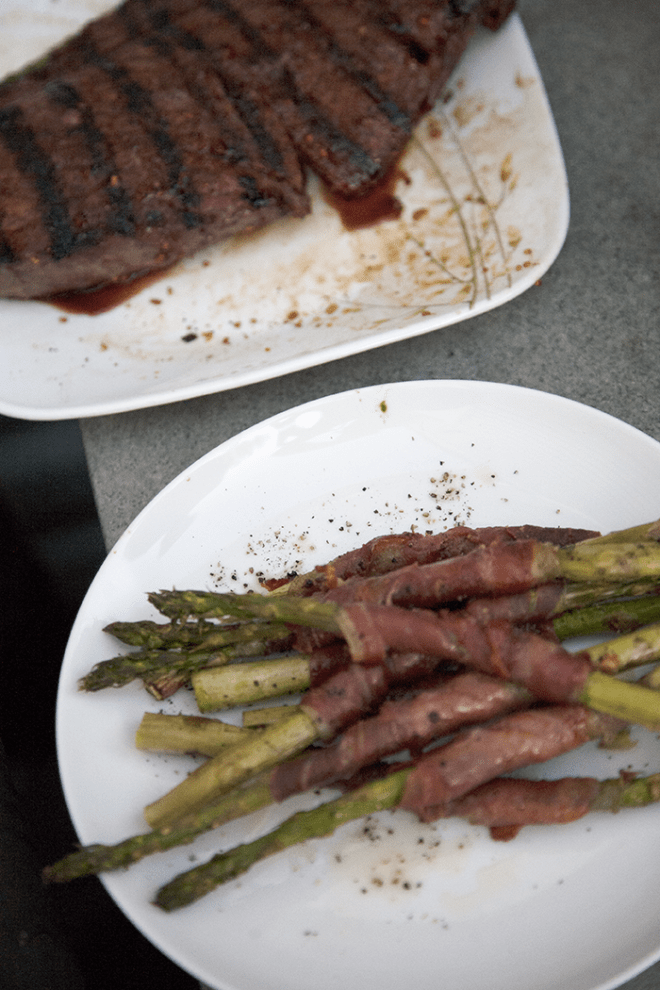 A plate of grilled steak and prosciutto-wrapped asparagus on a table.