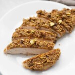 A plate of pistachio crusted chicken breast slices on a white background.
