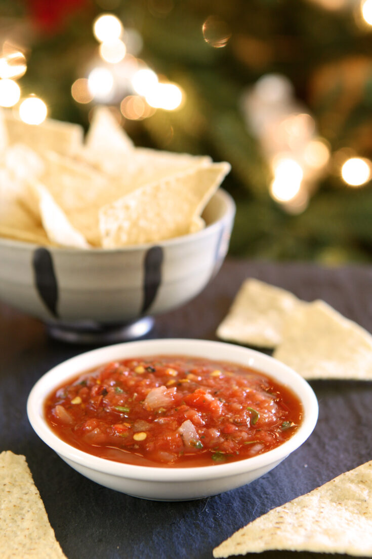Bowls of chips and salsa on a table in front of a lit Christmas tree.