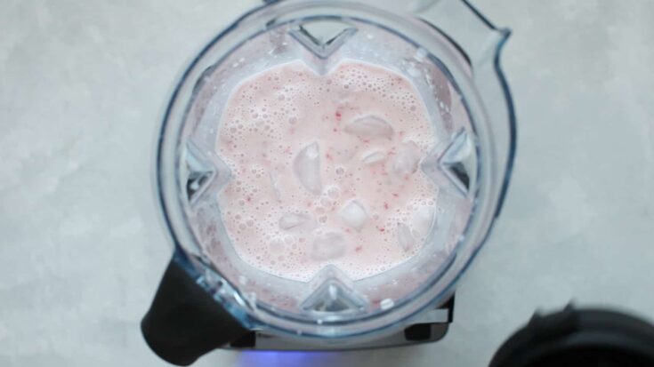 Overhead shot of a blender with the top off and ice added to the top of a smoothie.