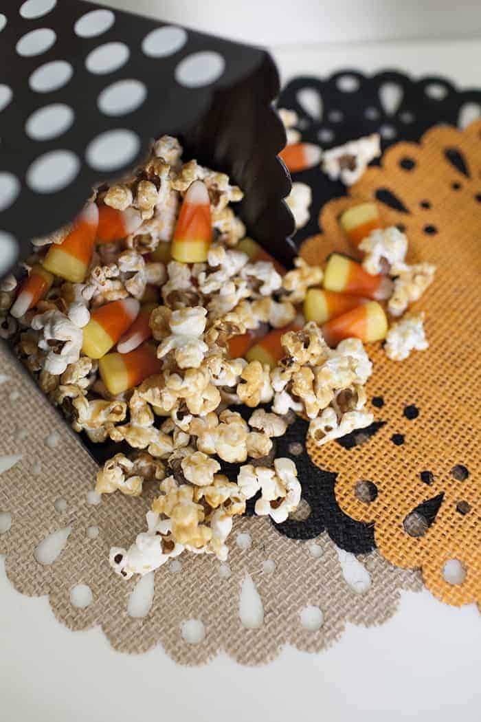 A bag filled with caramel popcorn and candy corn on top of a doily.