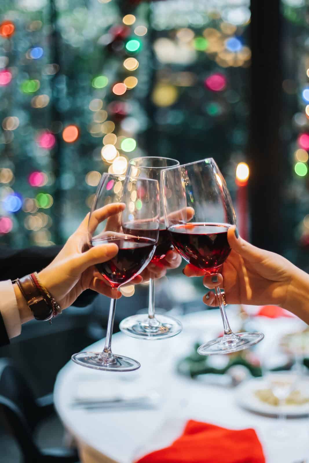 people toasting with red wine in front of a christmas tree