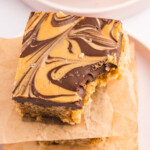 An exclusive close-up of a Rice Krispie Treat with a marbled chocolate peanut butter topping, a bite taken out of one corner, resting on parchment paper.