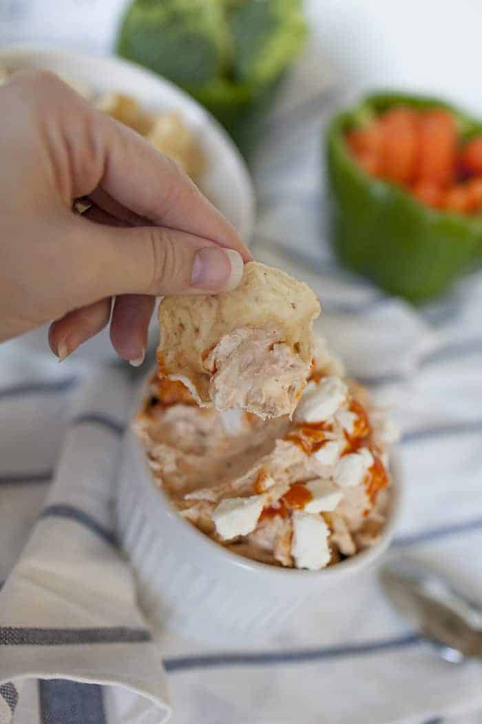 a hand dipping a tortilla chip into buffalo chicken dip.