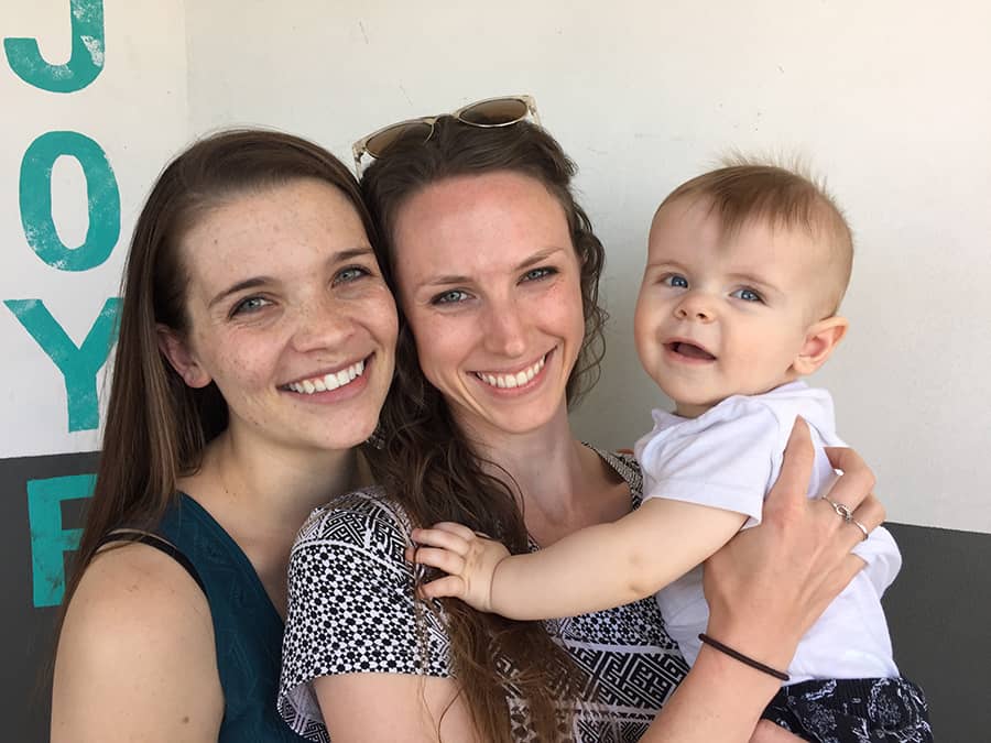 Three women holding a baby in front of a sign that says joy during their phoenix to sedona day trip.