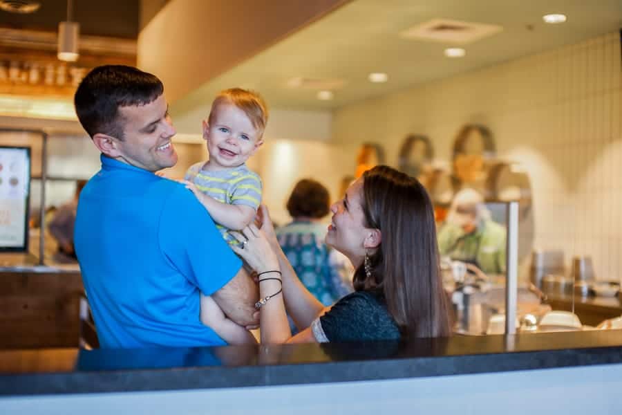 A man and woman holding a baby in front of a counter.