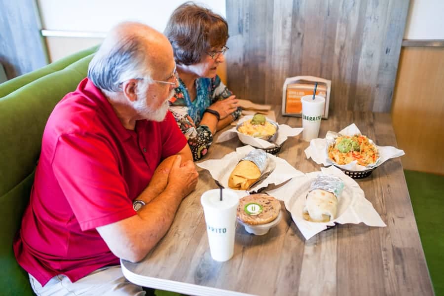 An older couple sits at a table with food in front of them.