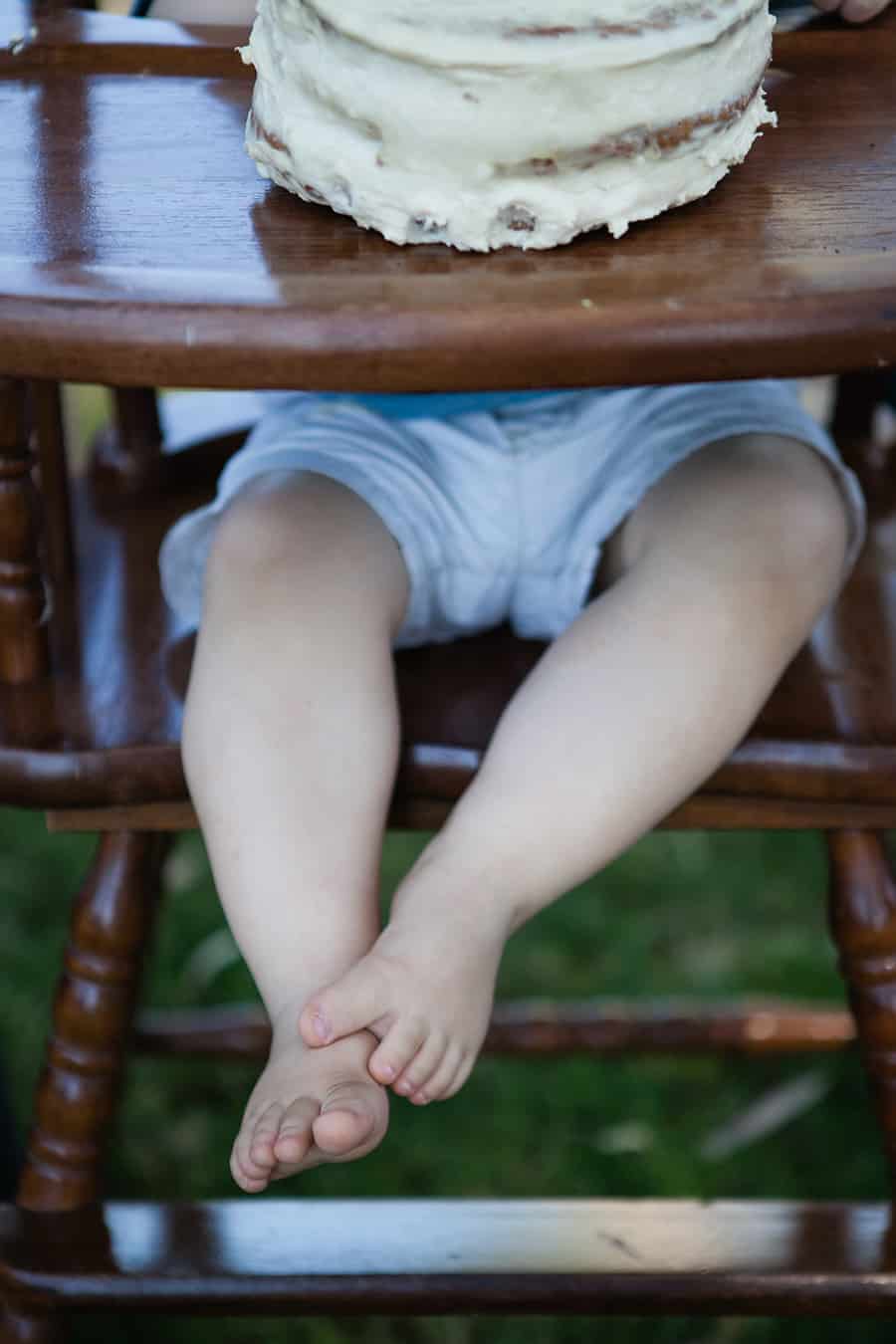 A baby sitting in a wooden high chair with a cake.