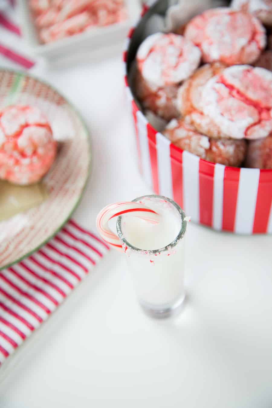 A glass of peppermint schnapps in front of a tin filled with crinkle cookies