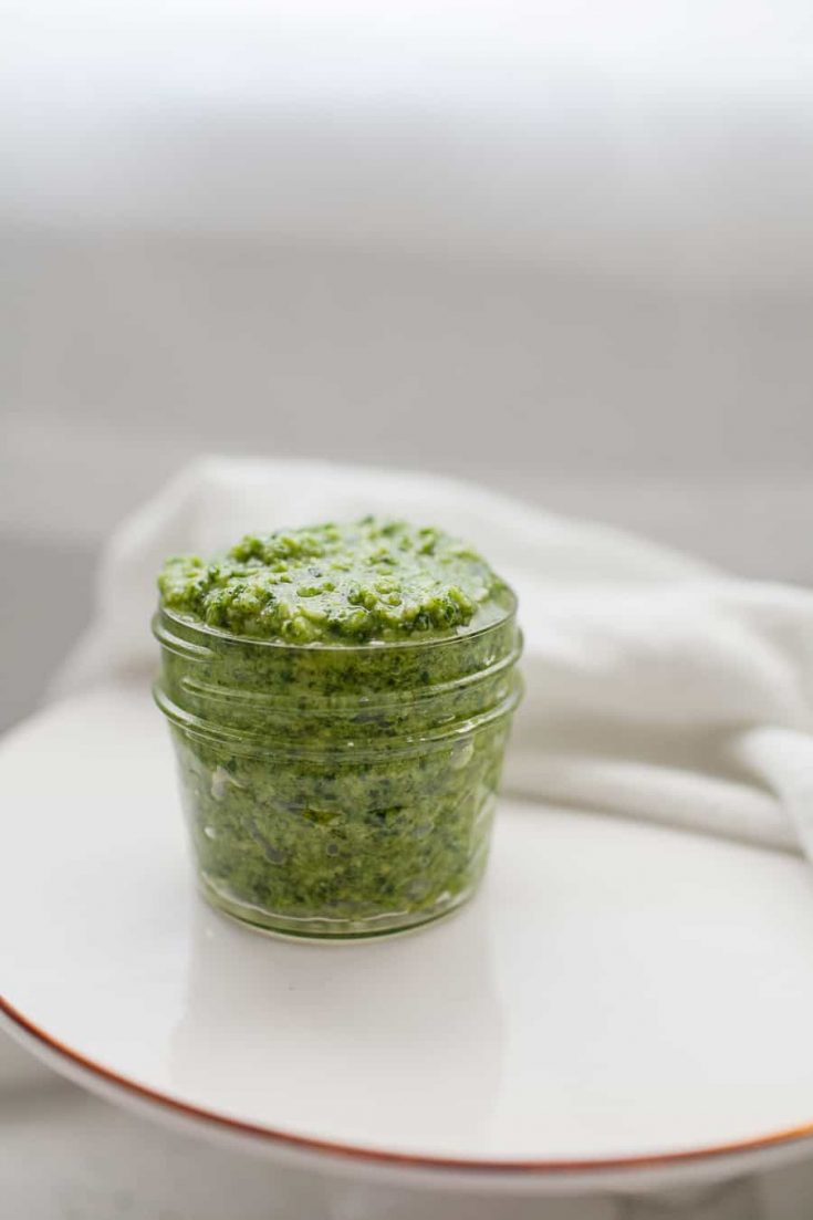 Fresh homemade kale arugula pesto in a glass jar on a white plate.