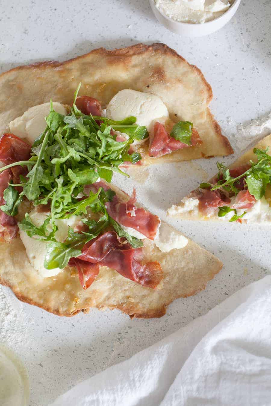 Overhead photo of prosciutto and ricotta thin crust pizza on the counter with a slice cut out from the main pie.