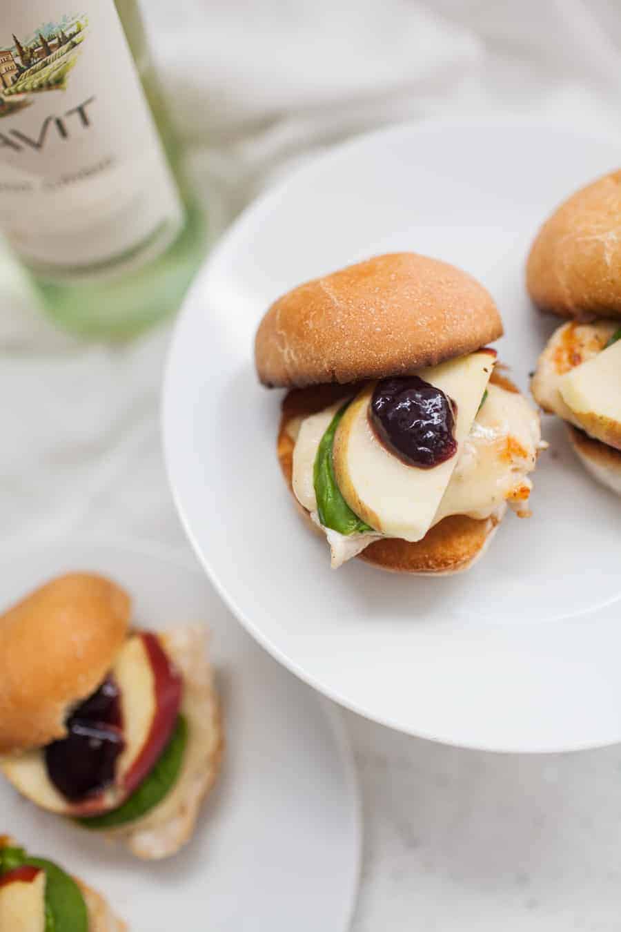 A plate with two chicken sliders topped with triple berry brie and a bottle of wine.