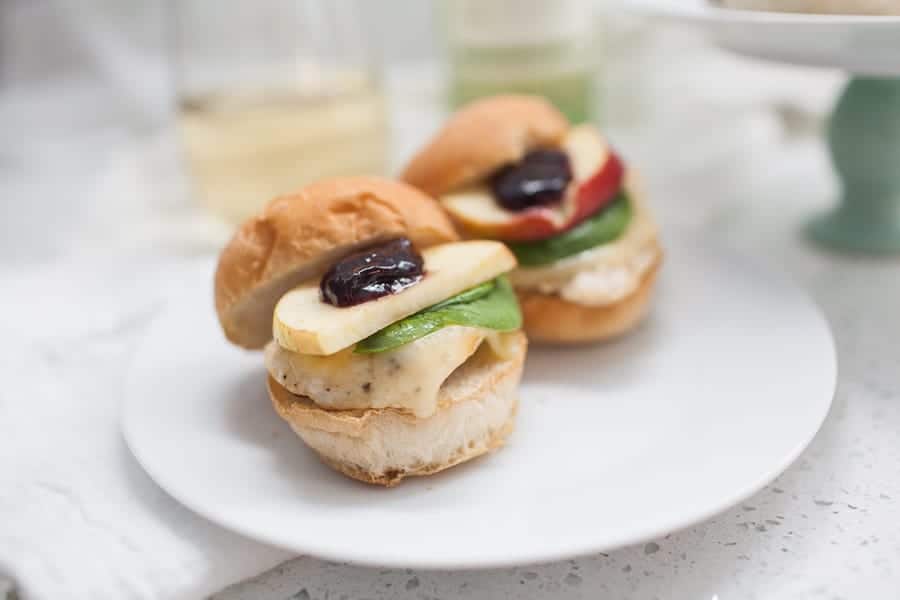 Two Triple Berry Brie Chicken Sliders on a plate next to a glass of wine.