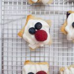 A tray of 4th of July cupcakes topped with whipped frosting and blue and red berries.
