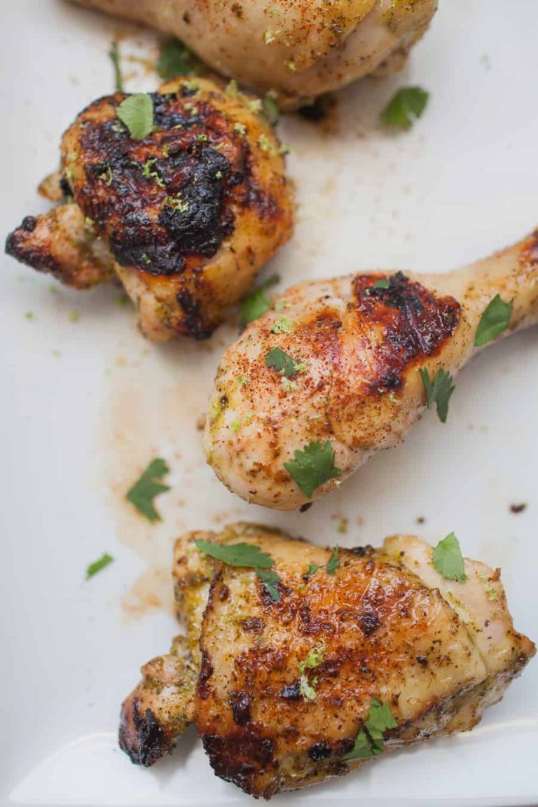 Three grilled chicken pieces, seasoned with a cilantro lime marinade and garnished with fresh herbs, served on a white plate.