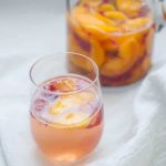 Peach raspberry sangria in a glass next to a pitcher.