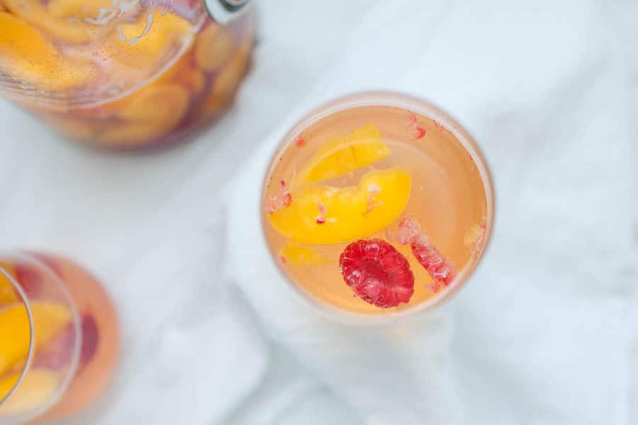 This Peach Raspberry Sangria is going to be the hit of all of your summer get togethers! A simple sangria recipe with peaches, raspberry, Moscato wine and a quick peach simple syrup makes this cocktail irresistible in the summer.?