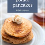 A stack of sweet potato pancakes topped with a dollop of whipped cream and a sprinkle of cinnamon on a white plate. A glass container of syrup is in the blurred background, reminiscent of summer mornings spent enjoying lemonade popsicles. Text reads "sweet potato pancakes joyfullymad.com".