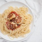 Baked chicken meatballs sprinkled with parmesan cheese on a bed of spaghetti with marinara sauce.