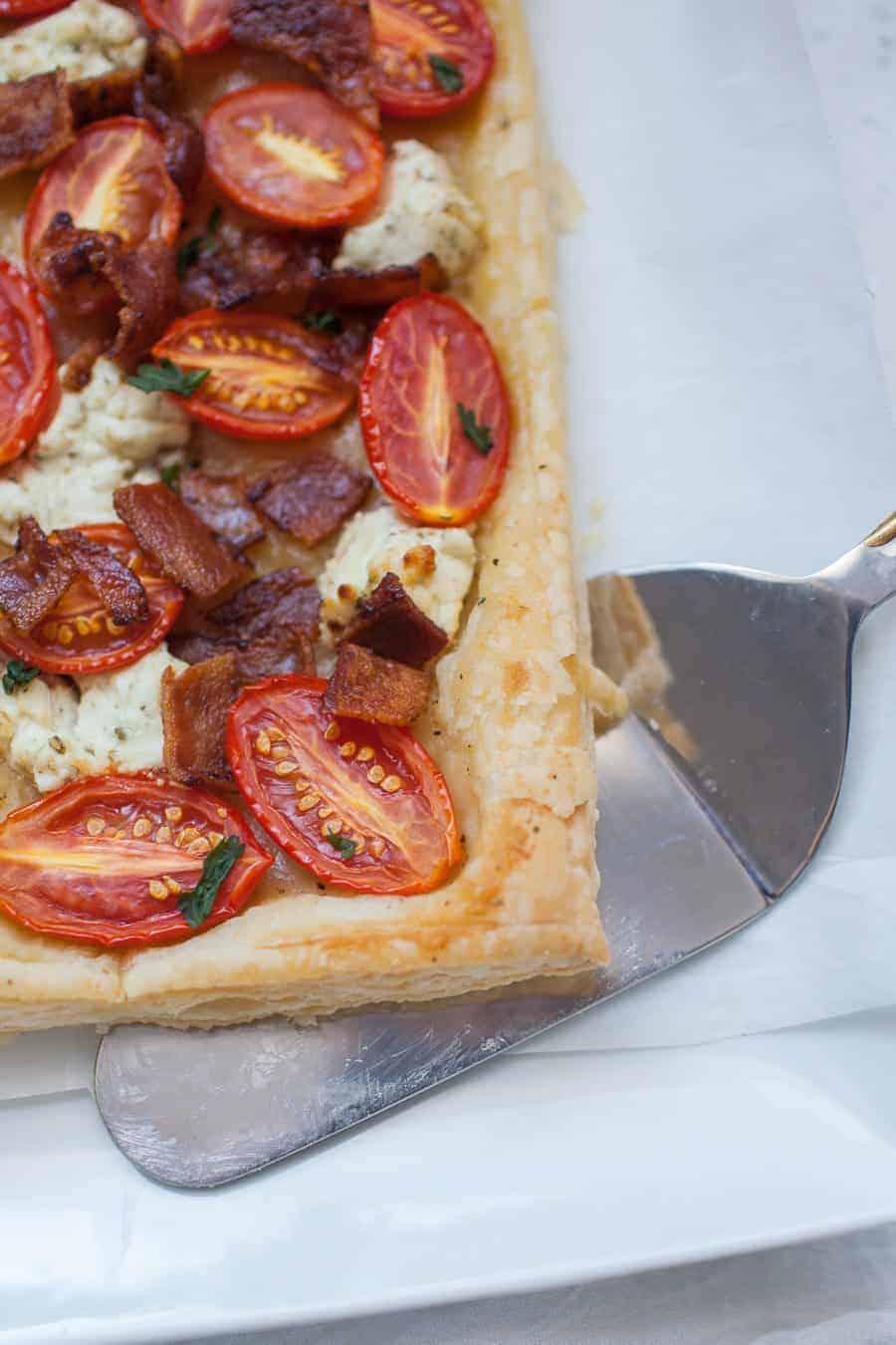 Tomato tart on a white rectangular serving plate with a pie server under the corner of the tart.