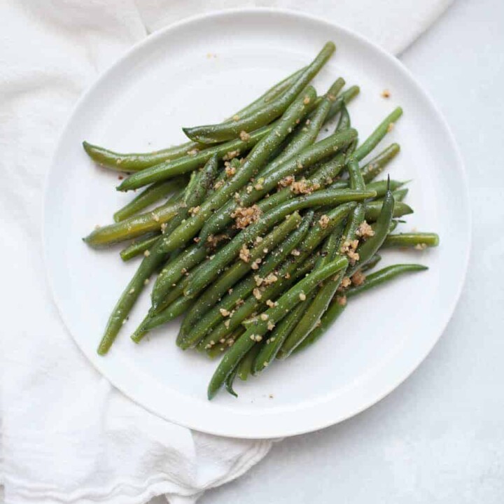 Overhead photo of garlic brown butter green beans on a white plate.