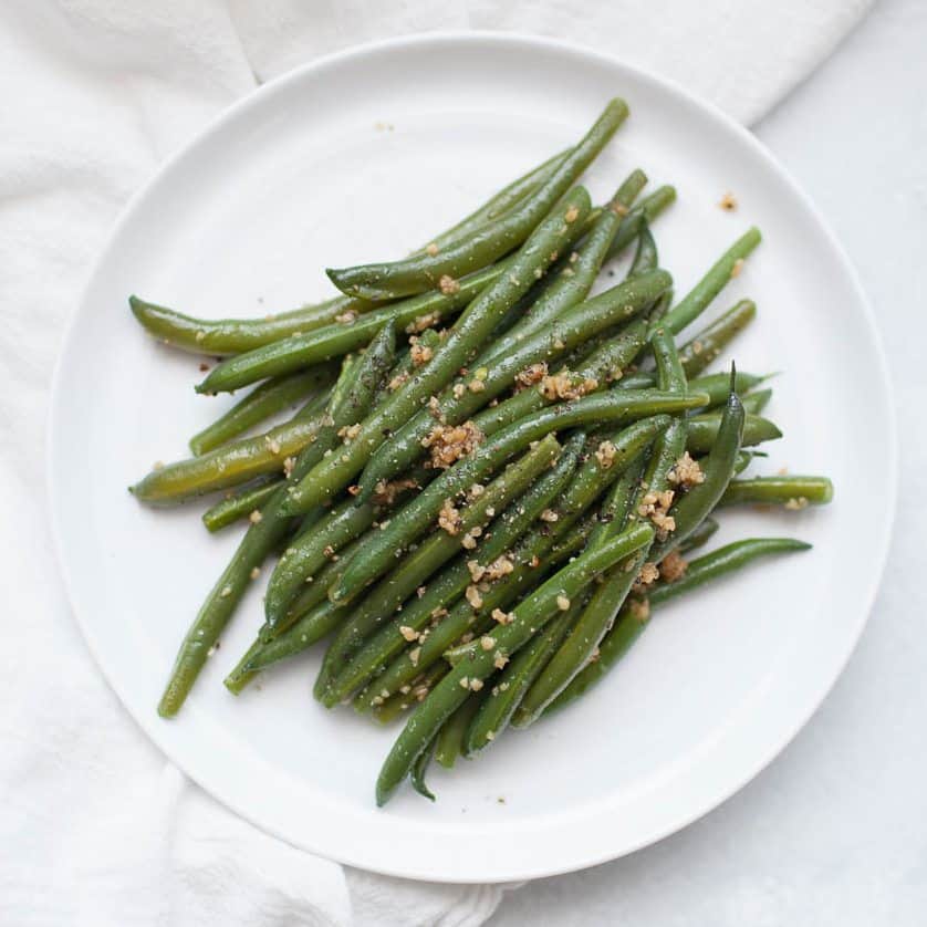 Garlic brown butter green beans on a white plate.