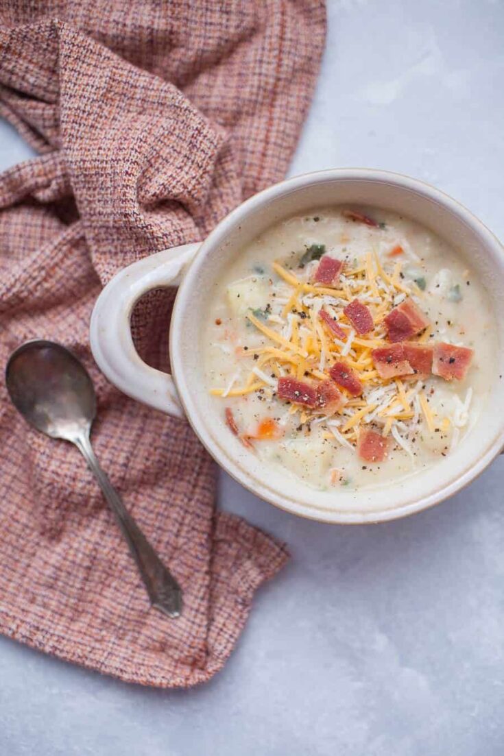 A white bowl of loaded baked potato soup with a red towel and a silver spoon. 