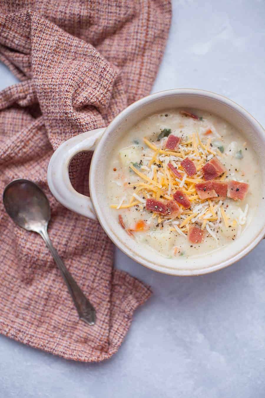 a spoon next to a white bowl containing baked potato soup. 