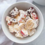 A bowl of fruit salad with mixed fruits, including banana slices and grapes, covered in a rich layer of whipped cream dressing.