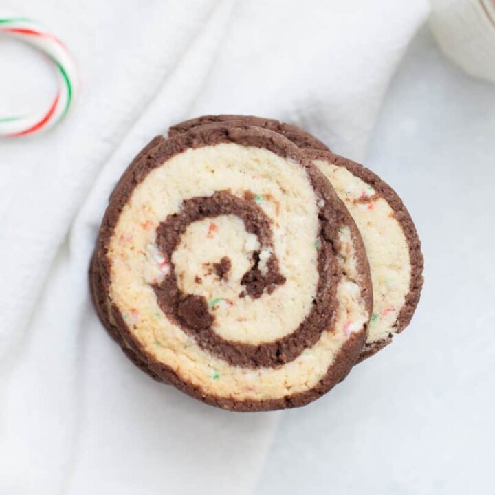 Chocolate Peppermint Pinwheel Cookies are the perfect cookie to share during the holidays! Two sheets of cookie dough, one that is smooth and chocolatey and one that is infused with peppermint and candy cane peppermint pieces, are rolled together to create these beautiful and festive pinwheel cookie slices. If you dream about the combination of peppermint and chocolate together during the holidays, these chocolate peppermint pinwheel cookies will be your new favorite Christmas cookie!