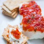 A stack of crackers next to pepper jelly on cream cheese, with one cracker topped with some of the cream cheese dip.