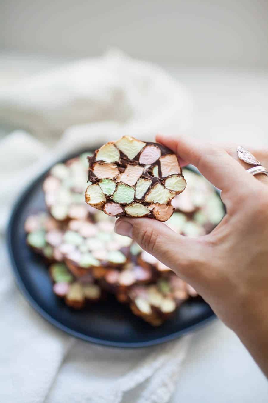 A female hand holding a cookie with colored marshmallows and chocolate.