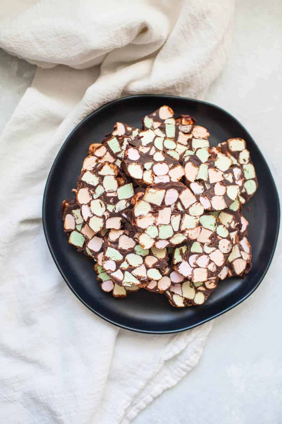 Dark gray stone plate with one inch thick stained glass window cookies, bright colored mini marshmallows and covered in chocolate.