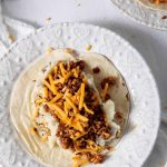 A plate of tacos with cheese, sour cream, and chorizo.