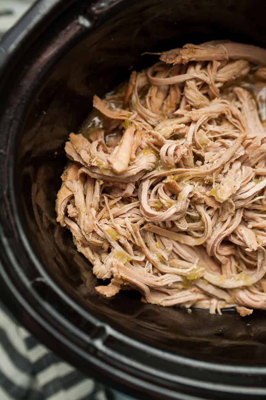 Tender, shredded cooked meat simmers inside a black slow cooker, perfect for crafting mouthwatering pulled pork tacos.
