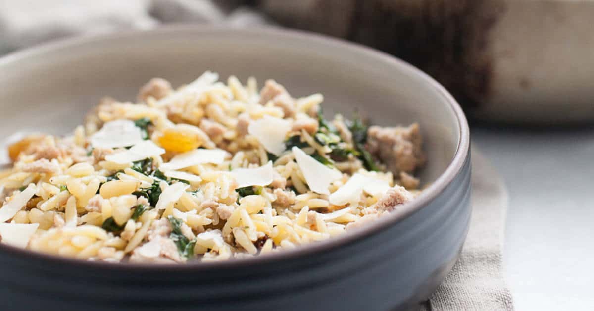 A bowl of orzo pasta with ground turkey, spinach, and shaved cheese.