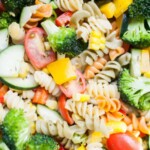 A colorful pasta salad recipe featuring rotini pasta, broccoli, cherry tomatoes, bell peppers, zucchini, and corn, all mixed together.