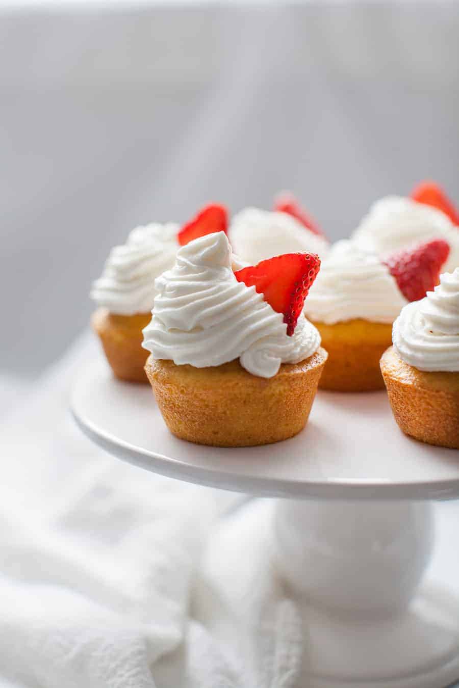 Strawberry shortcake cupcakes with whipped cream and strawberry garnish on cupcake stand.