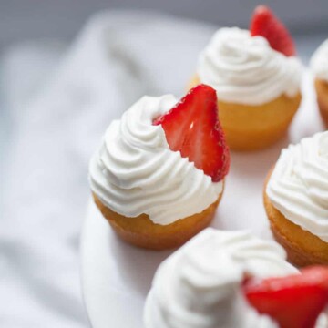 Close up photo of strawberry shortcake cupcakes with whipped cream and strawberry garnish on cupcake stand.