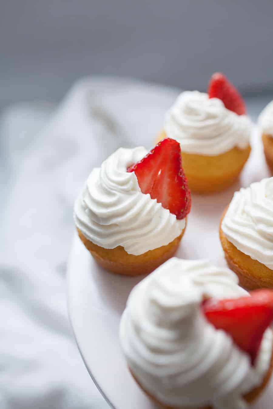 Close up photo of strawberry shortcake cupcakes with whipped cream and strawberry garnish on cupcake stand.