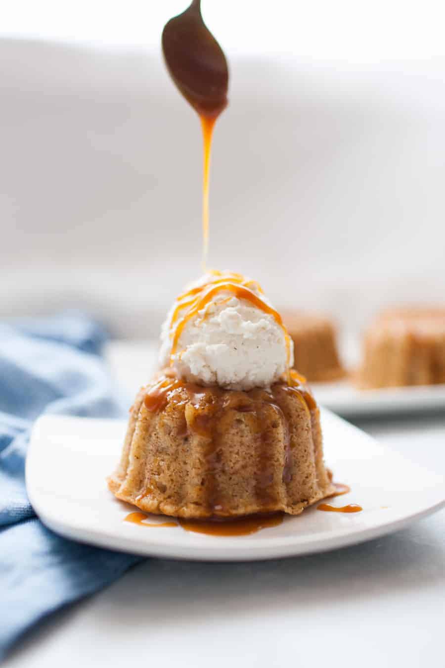 Pouring caramel sauce over mini bundt cakes topped with vanilla ice cream with a spoon.