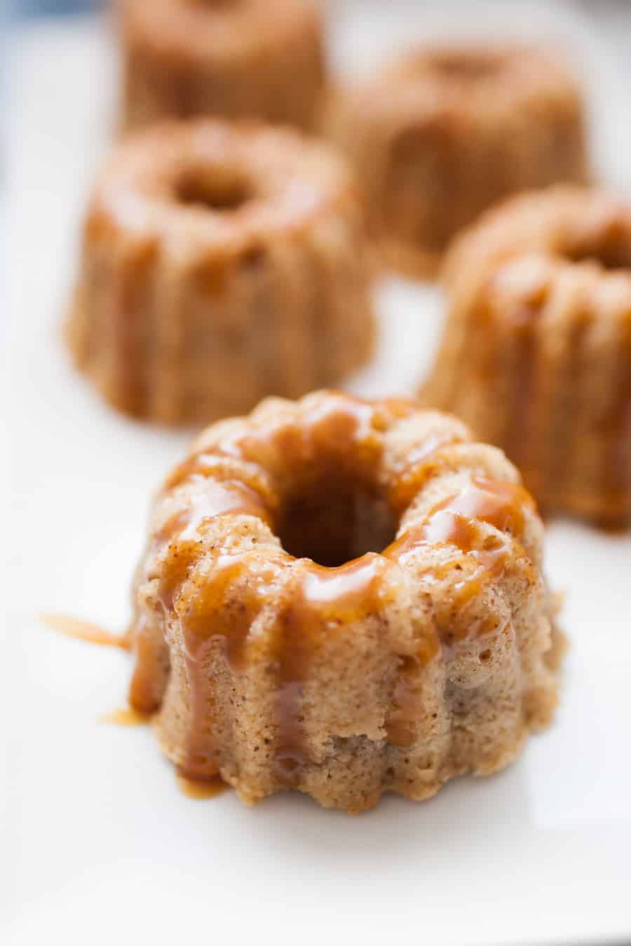 Mini bundt shaped cakes sitting on a white serving platter covered in homemade caramel sauce.