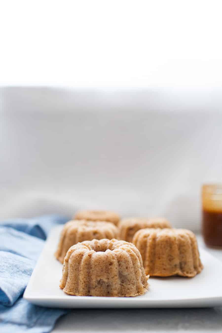 Mini bundt shaped cakes sitting on a white serving platter with small jar of caramel in the background.