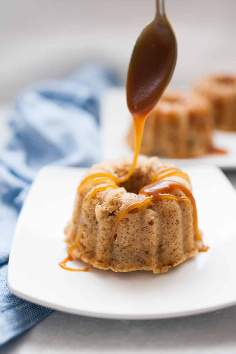 Pouring caramel sauce over mini bundt cakes with a spoon.
