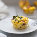 Egg Muffins with Sausage and Kale, served with fresh greens on a white plate and a fork, with another muffin blurred in the background.