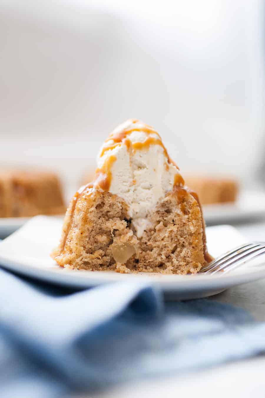 Mini spice cake that has had a bite taken out of it with a fork. Shows the inside of the cake with a scoop of ice cream and caramel drizzled on it.