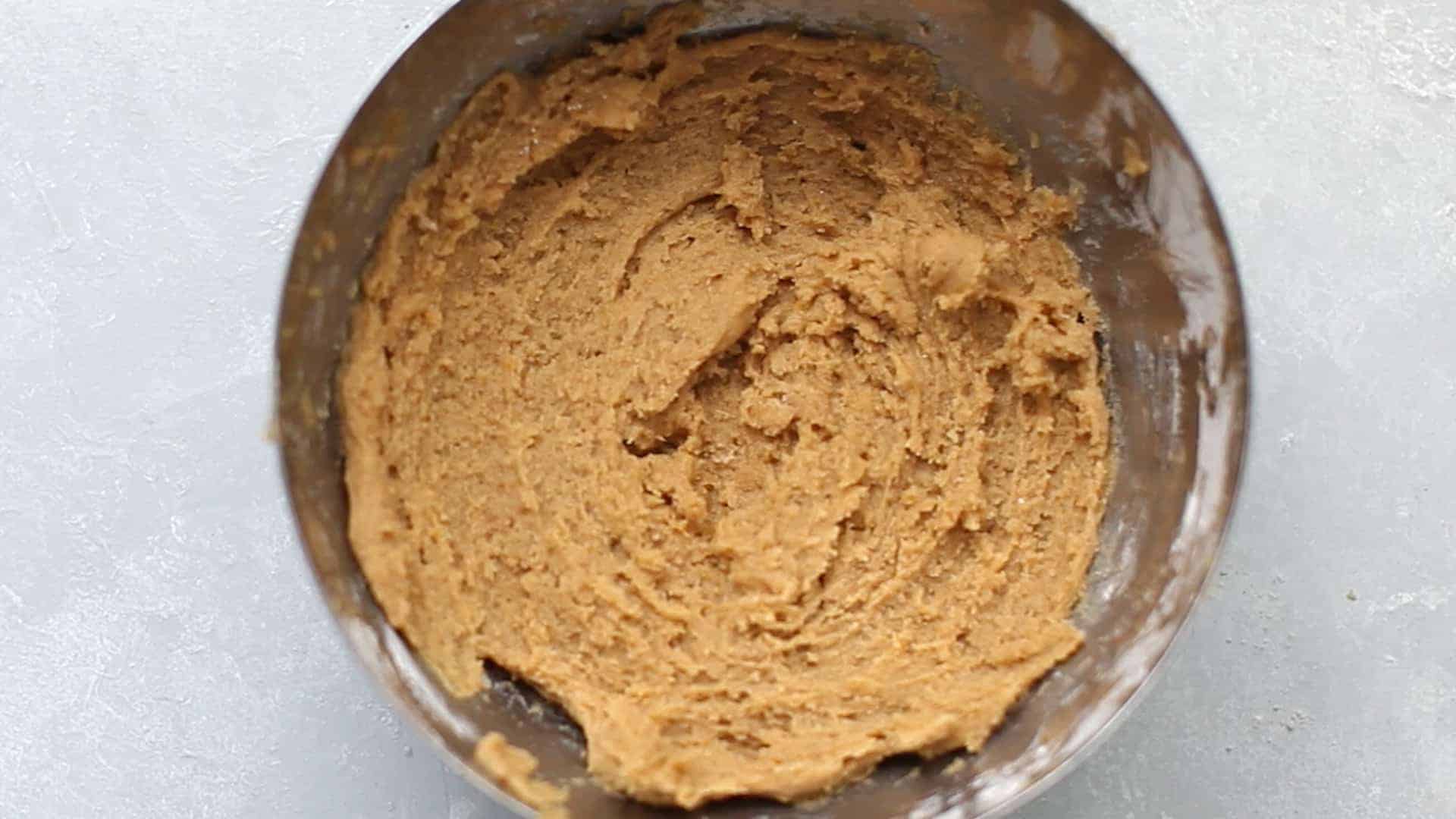 A stainless steel bowl with orange pumpkin snickerdoodle dough.