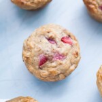 A close-up of a no-sugar muffin with visible strawberry pieces on a light blue background.