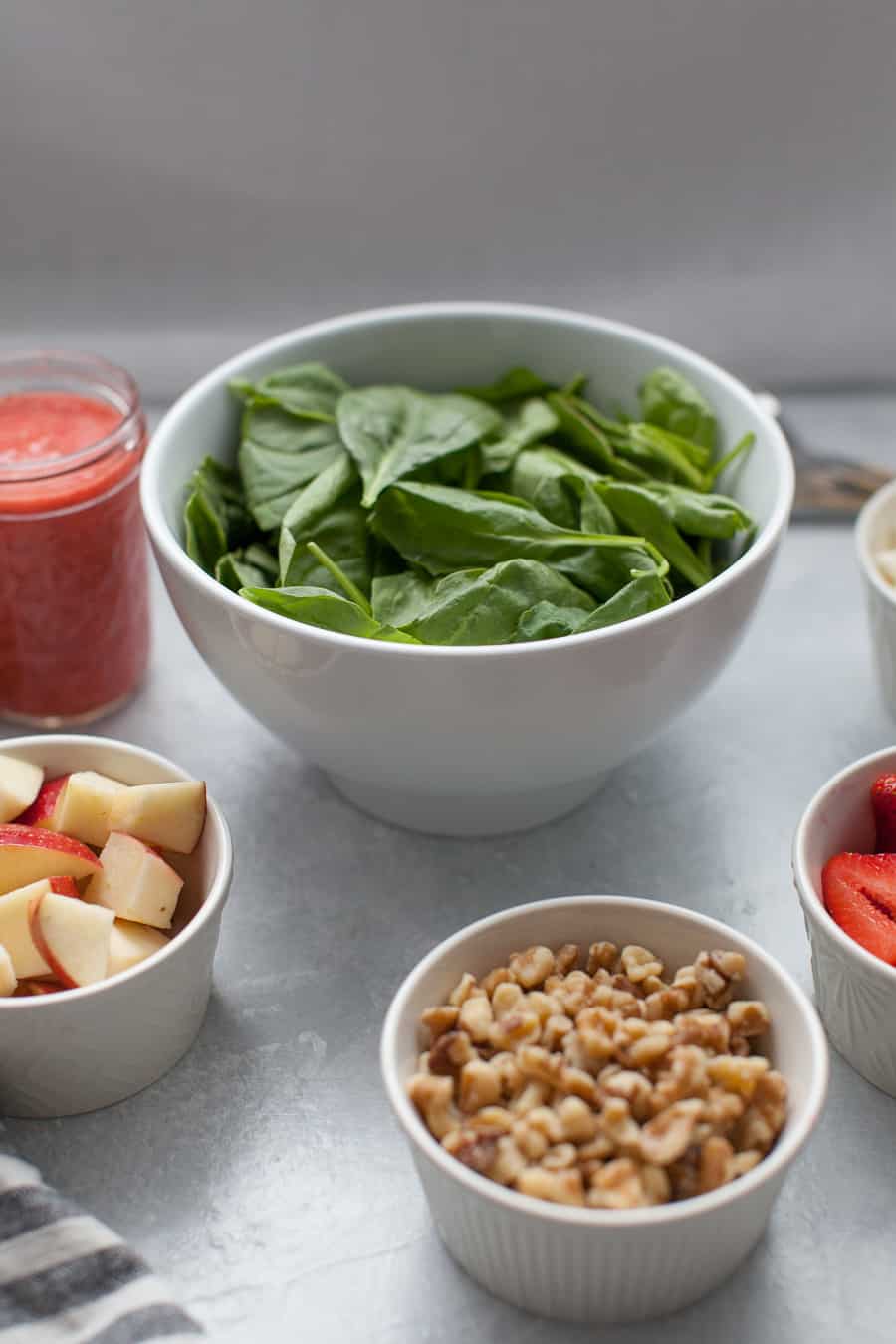 Bowls of spinach, apples, nuts, and a mason jar of strawberry vinaigrette.